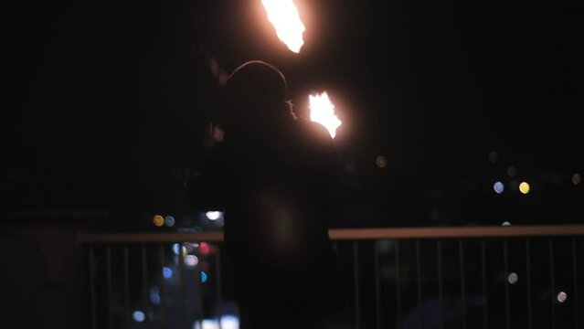 Fire dancer performing moves with fire poi on a rooftop of a building