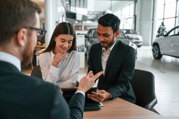 Man is buying automobile for his girlfriend. Three people are working together in the car showroom