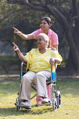 Indian caregiver nurse taking care of senior female patient in a wheelchair at park.