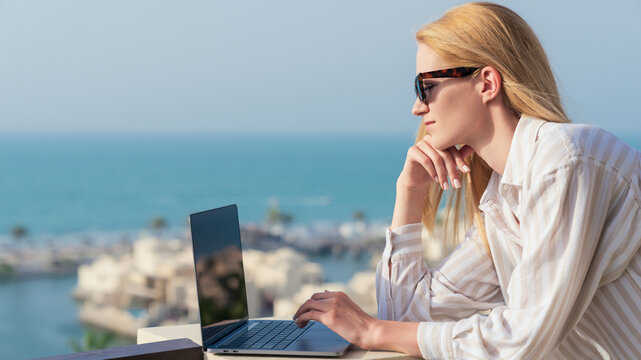 A female freelancer is working on a laptop with a sea view