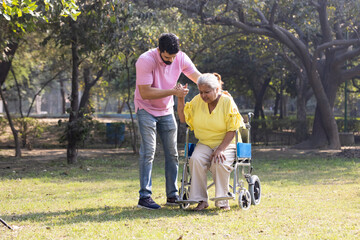 Male physical therapist discussing with senior woman in wheelchair at park.