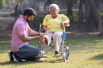 Male physical therapist discussing with senior woman in wheelchair at park.