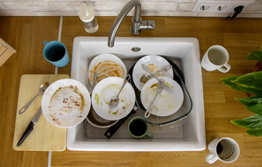 A pile of unwashed dishes in the sink. Mess and dirt in the kitchen. Dirty plates, mugs and cutlery. Putting the house in order, big cleaning, cluttered house.