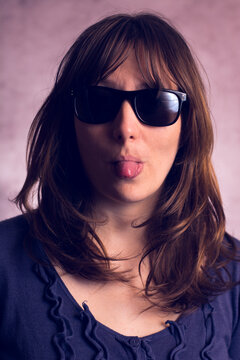 Face of a young model with long brown hair in sunglasses in the studio. Stretches out her tongue.