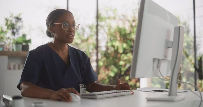 African Healthcare Nurse Using Desktop Computer for Day-to-Day Hospital Operations. Beautiful Young Clinic Professional Using PC for Online Medical Work in Modern Office in Public Health Care Facility