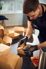 On the table. Man is packing food into the paper eco boxes. Indoors, restaurant