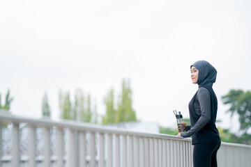 A young asian muslim woman wearing a black hijab is exercising and resting tired at the outdoor stadium in the morning. Modern Muslim woman concept,  Muslim woman sport concept, Islam