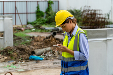 Female engineer in safety gear wearing hard hat using mobile phone at construction site