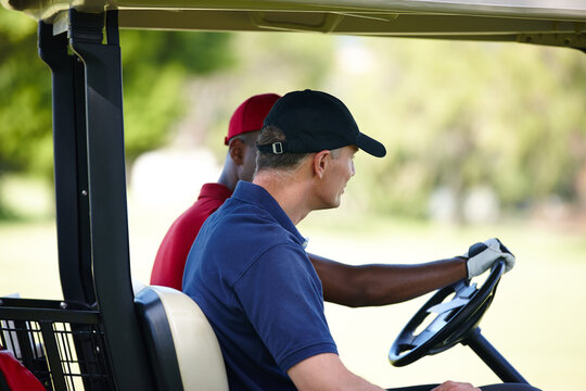 Carting it around the course. Profile of two men driving a golf cart on a golf course.