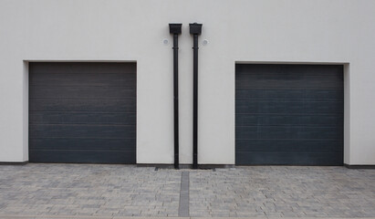 Two gray roller shutter garage doors on white facade. Clearance on pavement, driveway.
