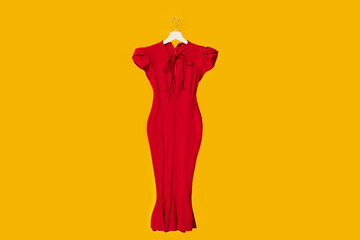 Bright beautiful classic elegant red dress on wooden hangers isolated on yellow studio background, free space