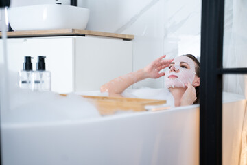 Young woman is lying in the bathroom, she has a face mask on her face. The girl is lying in the...