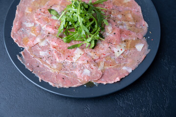 Marbled beef carpaccio with arugula, parmesan cheese, olive oil and lemon. A traditional classic appetizer made from thinly sliced raw meat. Close-up, selective focus, top view, black background.