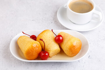 Neapolitan Rum baba (or baba au rum) on a white plate with a cocktail cherry and a cup of coffee. Small yeast cakes soaked in rum syrup on a gray background. Traditional Italian pastry. 