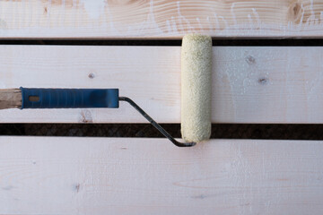White paint roller applicator brush with handle painting wooden fence, floor plank. Cosmetic repair, house renovation