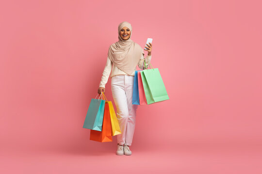 Smiling Muslim Woman Walking With Smartphone And Shopping Bags In Hands