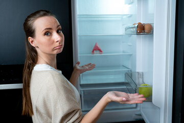 Fototapeta na wymiar Young woman in the kitchen looks inside an empty refrigerator without food. 
