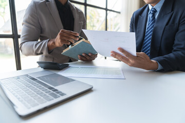 Obraz premium Two young Asian businessmen analyzing Calculate and discuss and brainstorm data, charts, graphs Taking notes on financial reports in notebooks at office financial advisors and accounting concepts.