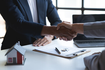 Two young Asian businessmen shake hands after signing a contract to invest in a village project. real estate, with businesswomen joining in showing joy and clapping in the office.
