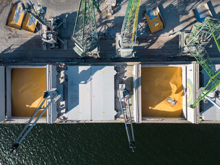 Aerial view of a bulk carrier ship loaded with grain is docked at a busy port, with workers and...