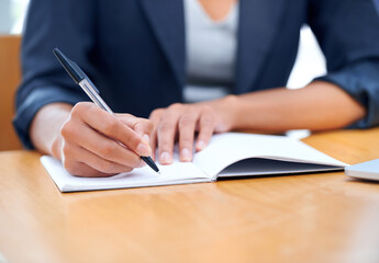 Meeting minutes. A businesswoman making notes in a notebook while sitting at a desk.