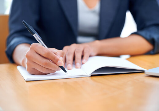 Meeting minutes. A businesswoman making notes in a notebook while sitting at a desk.
