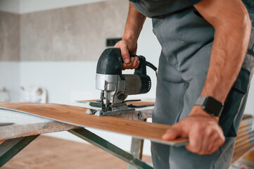 Using the electric machine tool to cut the plank. Man is installing new laminated wooden floor