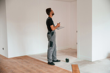 Making notes into the document and using laser leveler. Man is installing new laminated wooden floor
