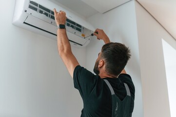 Man repairs an air conditioner indoors at home