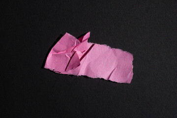 Pink crumpled torn paper piece isolated on a black background. Ripped blank paper with copy space...