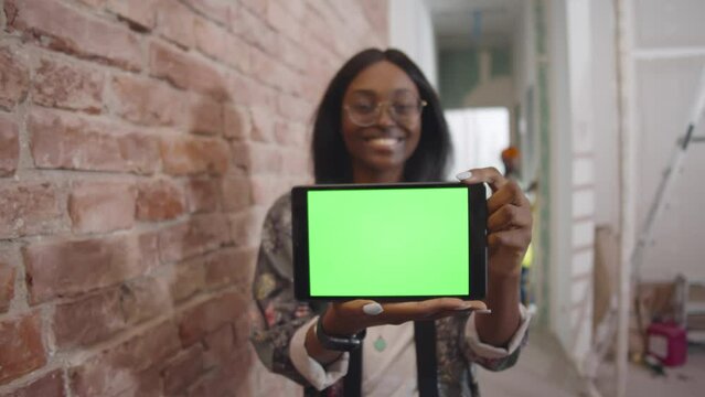 Woman show green screen tablet computer and smile at camera at construction site. Realtime