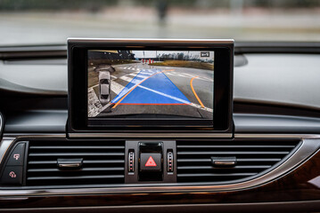 Multimedia screen in car, rear view camera, emergency button. Interior of premium car with camera dynamic trajectory turning lines and parking assistant steering wheel turned right. Details closeup.