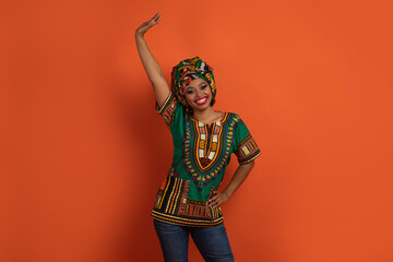 Positive funny black woman in african costume dancing on orange