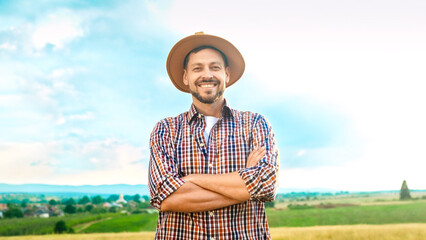 Portrait shot of handsome Caucasian cheerful man in motley shirt and hat standing in field on...