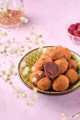 Homemade chocolate truffles with dried cherries in a ceramic bowl on a pink concrete background.