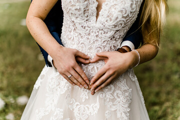 Ehepaar hält Hände in Herzform vor den Bauch der Braut