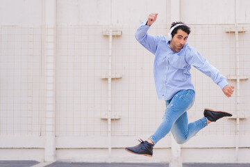 Middle aged latin man jumping with happiness in the city while wearing headphones. Copy space.