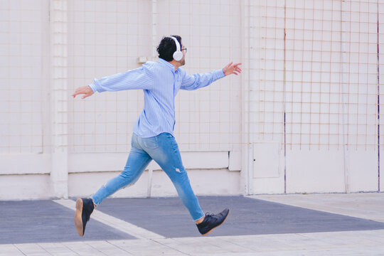 Young latin man running pompously in the street while wearing headphones. Copy space.