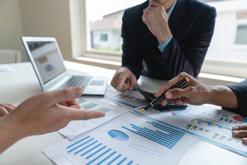 A group of Asian businessmen are brainstorming to analyze financial reporting situations. Calculate investments, income, taxes, accounts from data reference graphs. Income from laptop at office desk.