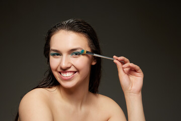 Obraz premium Happy young woman with perfect skin, long brunette shiny hair and beautiful smile posing over grey background. Beauty, skin care, cosmetology, spa, ad concept