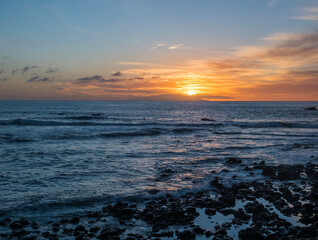 Pink orange golden sunset with waves at a black sand beach with lava stones and rock, Sun setting to the atlantic ocean. La gomera island, Canary Islands