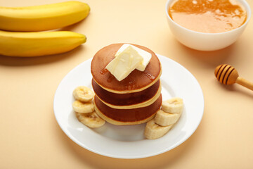 Plate with yummy banana pancakes on beige background.