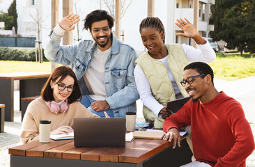 Smiling young multiethnic people students studying with laptop together, wave hand, say hi,...