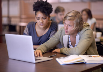 Obraz premium Getting through the work together. Two students researching their assignments together on a laptop.