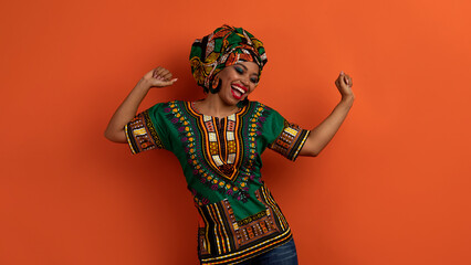 Joyful pretty black woman in african costume dancing on orange