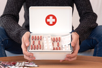 Crop male in casual clothes sitting at home and showing many medications in white first aid kit...