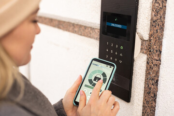 Woman locking smartlock on the entrance door using a smart phone. Concept of using smart electronic locks with keyless access.