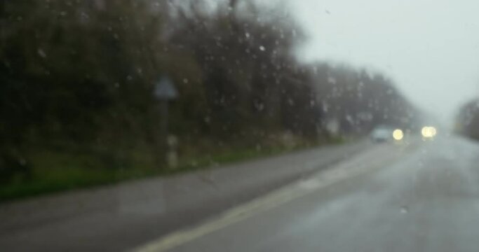 Defocused blur view of multiple cars driving on wet asphalt on a heavy rain - close up 4K DCI footage in the car windshield