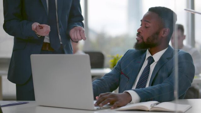 Young African-American office manager sit at desk being reprimanded by boss