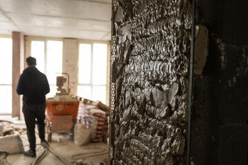 Fototapeta premium Construction worker wearing worker overall with wall plastering tools renovating apartment house. Plasterer renovating indoor walls and ceilings with float and plaster. Construction finishing works.
